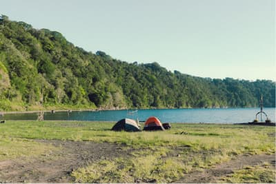 Beberapa tenda didirikan di tanah lapang di tepi danau dengan permukaan air tenang dan pepohonan di kejauhan