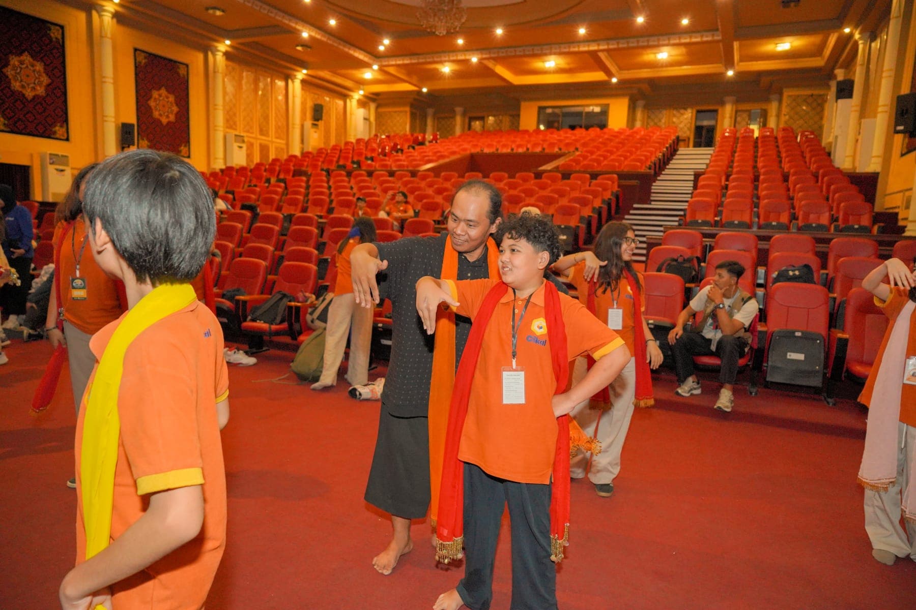 Puluhan siswa mengenakan selendang oranye berdiri berbaris di dalam auditorium sambil mengangkat tangan bersama
