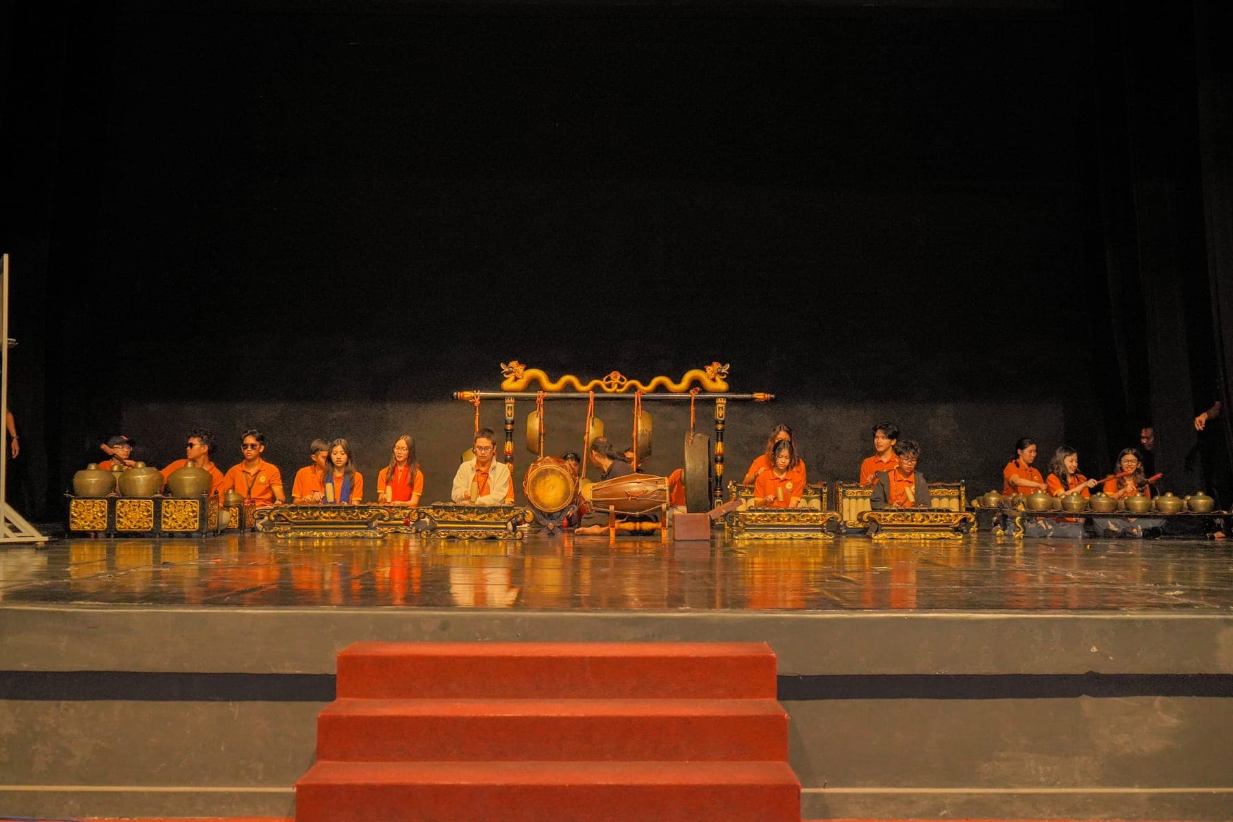 Sekelompok penabuh gamelan duduk bersila di belakang perangkat bonang dan saron di atas panggung berlampu hangat