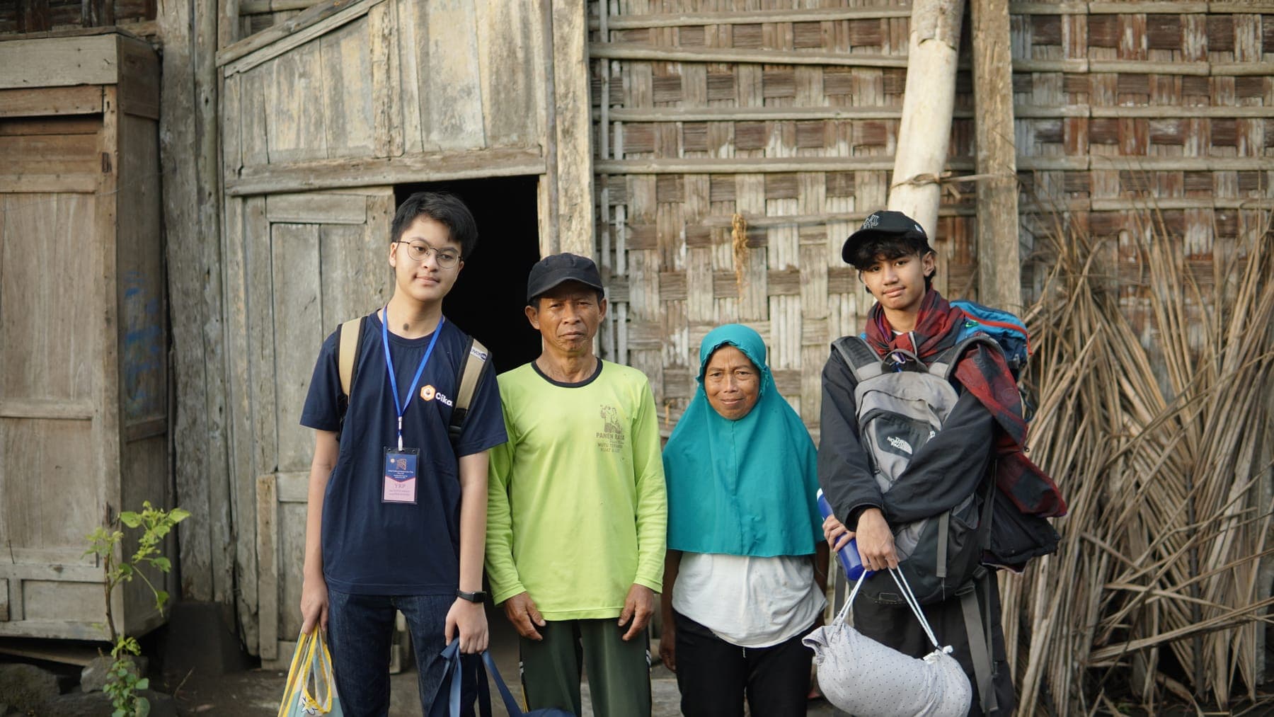 Sekelompok siswa berseragam duduk bersama anggota keluarga penerima di teras rumah desa